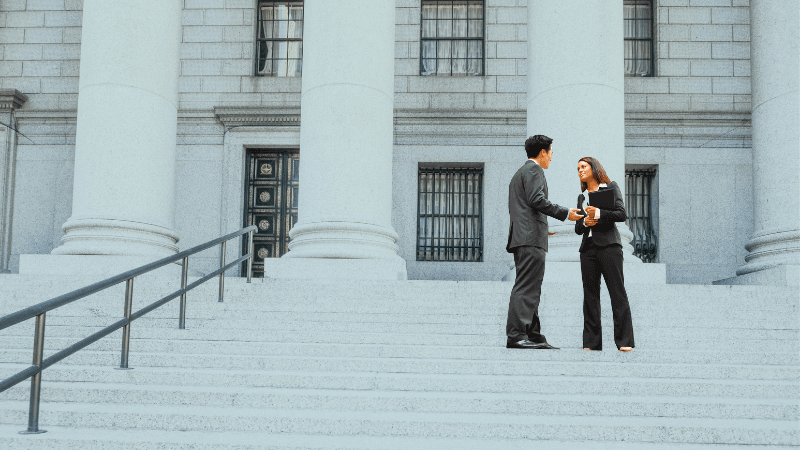 Two Judicial Law Clerks Discussing A Case Outside A US Courthouse A Year In Chambers Could Be Worth $180,000 To The Right Firm