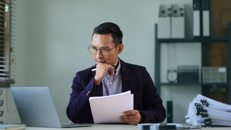 Man Looking At Laptoop Holding Documents